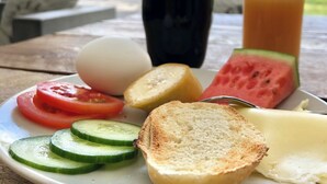 A plate of food with a slice of watermelon, a tomato, cucumber slices, a boiled egg, and toasted bread, along with a black cup and a glass of iced tea. - Gothem Logi (Slite)