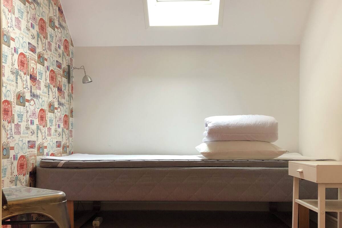A small, neatly arranged room with a single bed, a desk, and a chair.