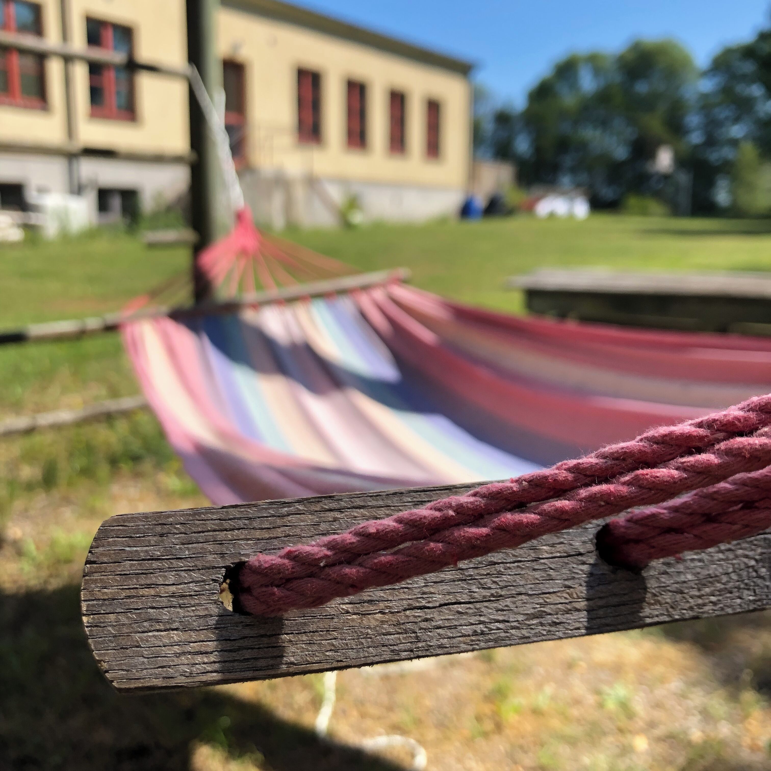 A hammock tied to a wooden post in a grassy area with a building in the background.