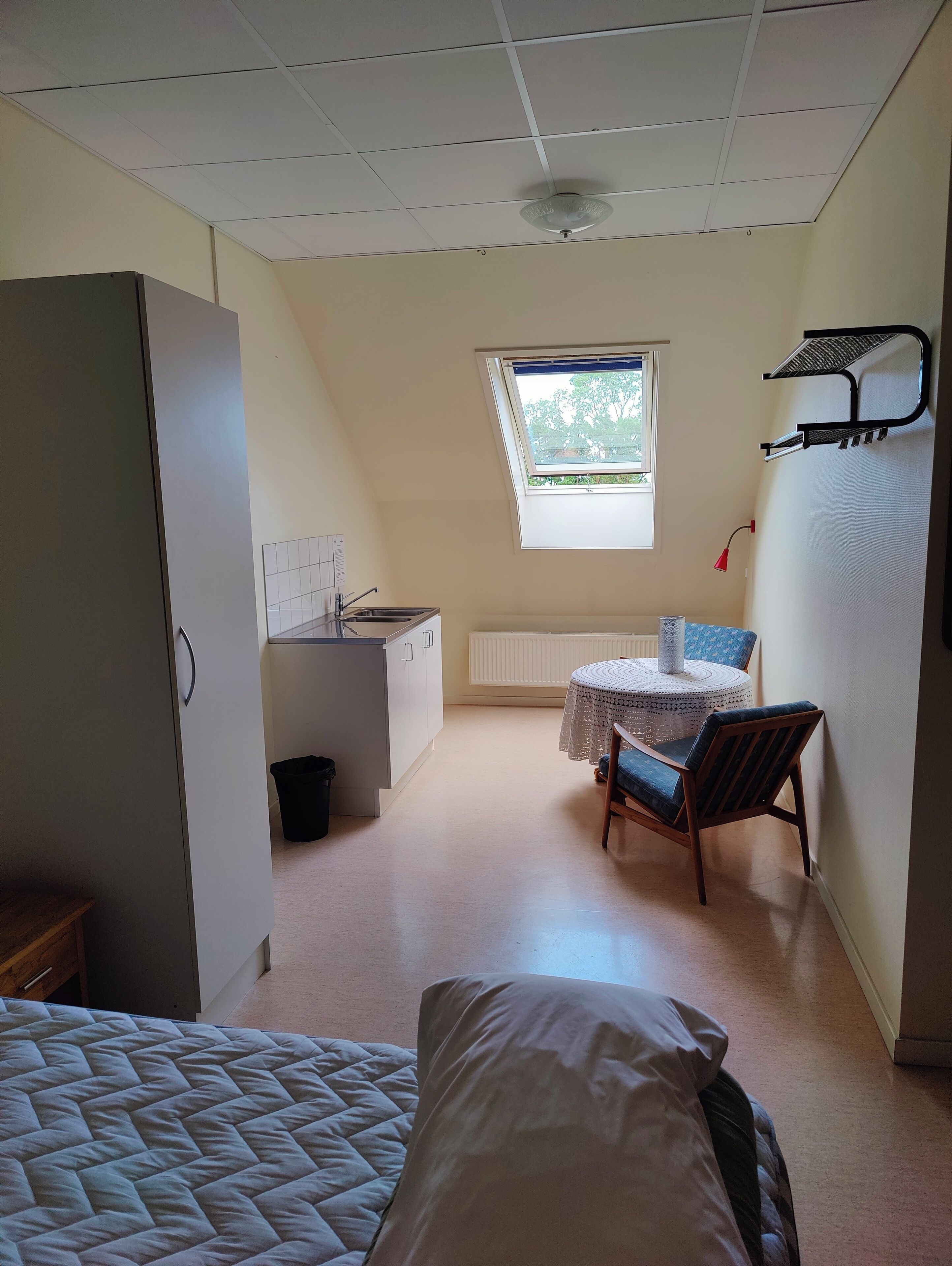 A compact room with a kitchenette, a dining area with a table and chairs, a bed, and a window providing natural light.