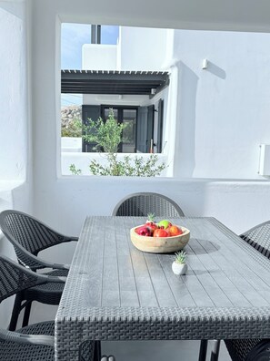 Un comedor con una mesa, sillas, un bol de fruta y vistas a un edificio a través de una ventana.