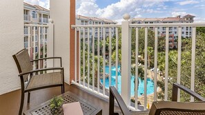 En balkon med udsigt til en swimmingpool, omgivet af palmer og en bygning.