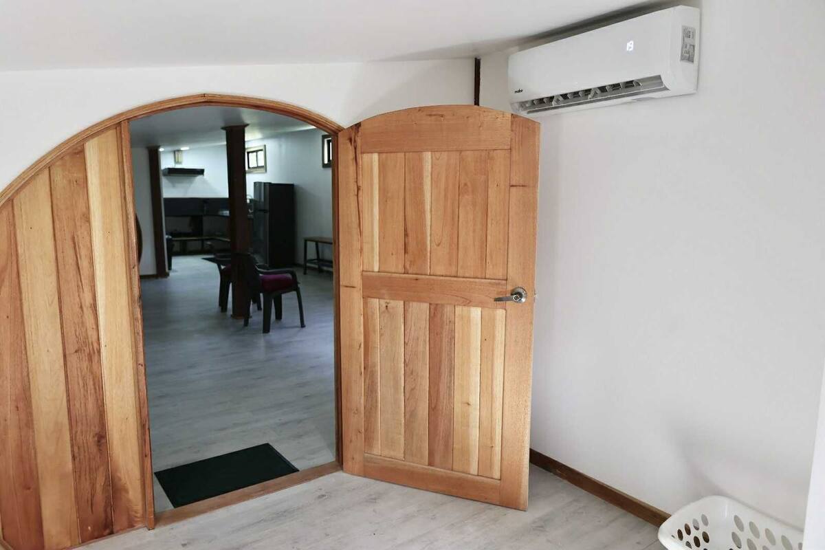 Puerta de madera abierta que da a una habitación con un aire acondicionado blanco instalado en la pared.