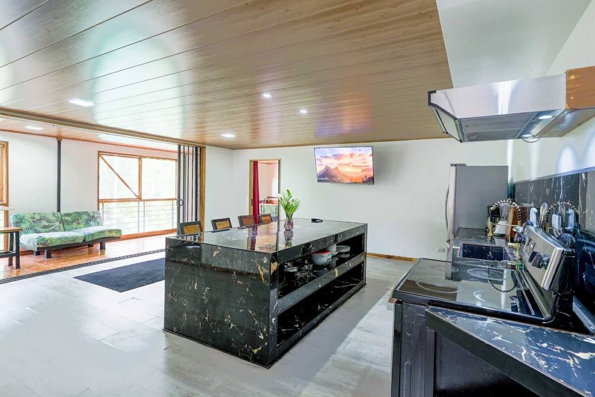 Una cocina moderna con una isla de mármol, un rincón de comedor con sofá y un amplio ventanal.