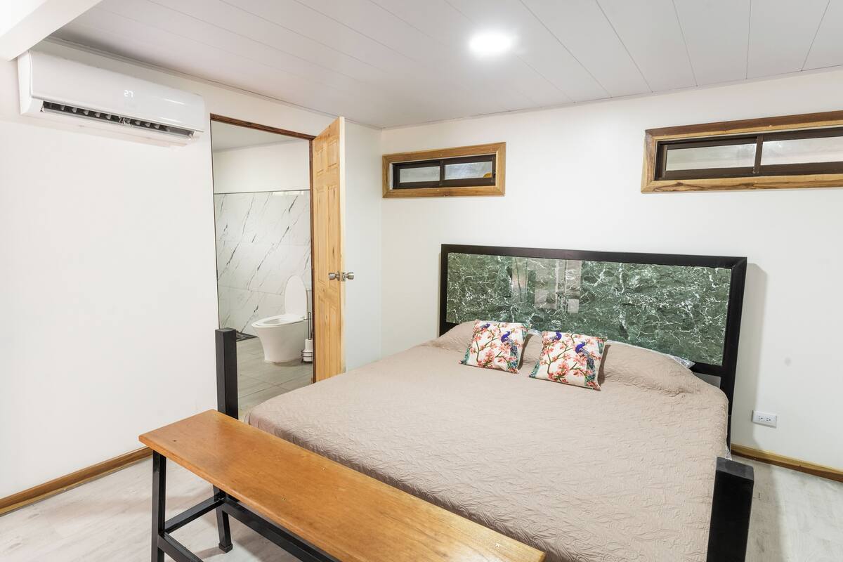 Un dormitorio con una cama, un banco, una puerta de madera y una ventana.