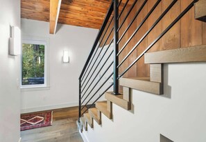 Un escalier avec des marches en bois et des rampes en métal noir, menant à un palier doté d’une fenêtre donnant sur un espace verdoyant.
