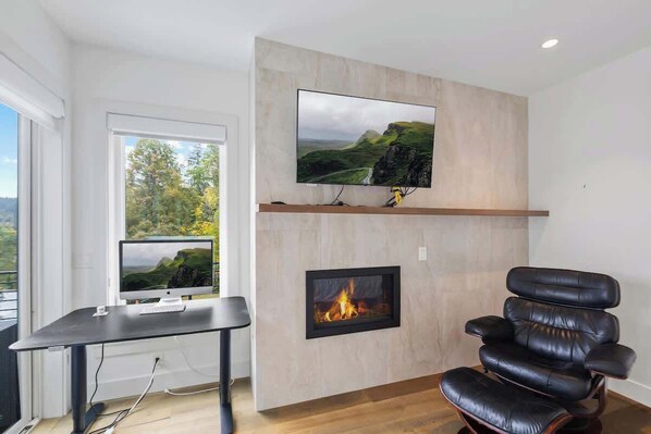 Un salon moderne avec une cheminée, un téléviseur fixé au mur et un fauteuil en cuir confortable.