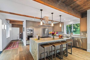 Une cuisine moderne dotée d’un grand îlot central, d’appareils électroménagers en acier inoxydable et de poutres en bois.