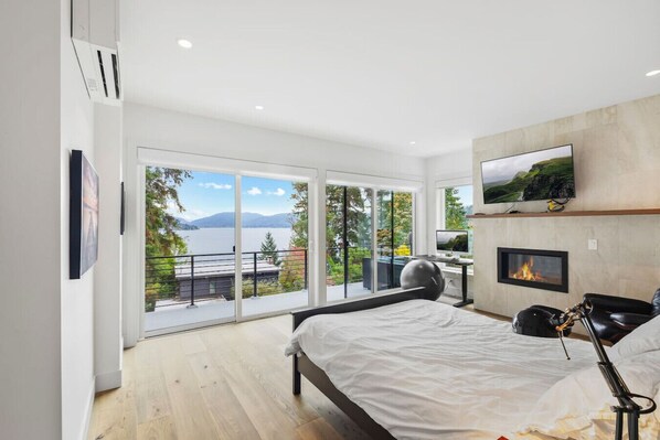 Un dormitorio moderno con una cama grande, televisión, chimenea y balcón con vistas panorámicas.