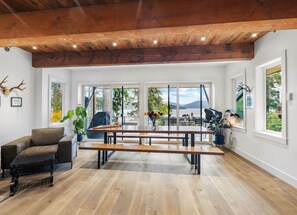 Amplia sala de estar con un banco de madera, un sofá y una mesa de comedor. Grandes ventanas ofrecen vistas al exterior.