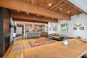 Un amplio salón con techo de madera, una cocina al fondo y una gran mesa de comedor de madera.