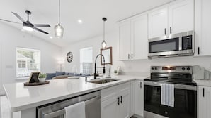 A modern kitchen with white cabinetry, a stainless steel oven, a microwave, and a ceiling fan. - Family Getaway: Pet Friendly • Close to Downtown (St. Augustine)