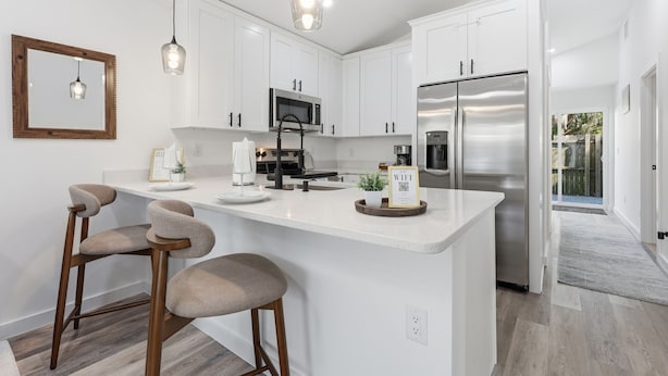 A modern kitchen with white cabinets, stainless steel appliances, and a central island with bar stools. - Family Getaway: Pet Friendly • Close to Downtown (St. Augustine)