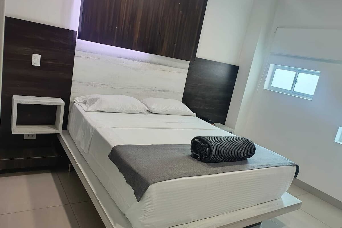A modern bedroom with a bed, a small bedside table, and a window.
