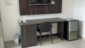 A hotel room with a wooden desk, a chair, a small refrigerator, a TV mounted on the wall, and a bed with a rolled-up towel. - HOTEL SAN ANTONIO PLAZA APARTADO (Apartadó)