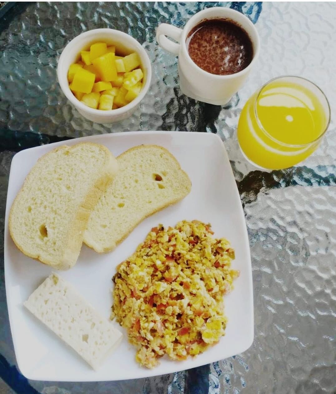 A breakfast plate with toast, scrambled eggs, and a glass of orange juice on a glass table.