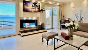 Ein geräumiges Wohnzimmer mit einem großen Fernseher, einem bequemen Sofa, einem Couchtisch und Meerblick durch große Fenster.