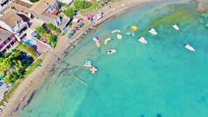 Ein Luftbild einer Strandbucht mit klarem türkisblauem Wasser, mehreren Booten und einer Reihe von Strandsonnenschirmen.
