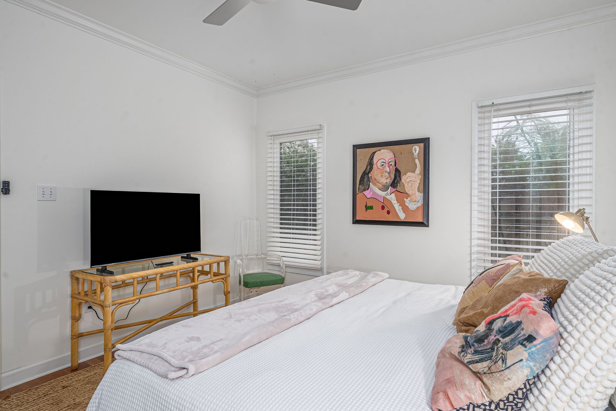 Une chambre à coucher avec un lit, un téléviseur posé sur un meuble, une chaise et un tableau accroché au mur.