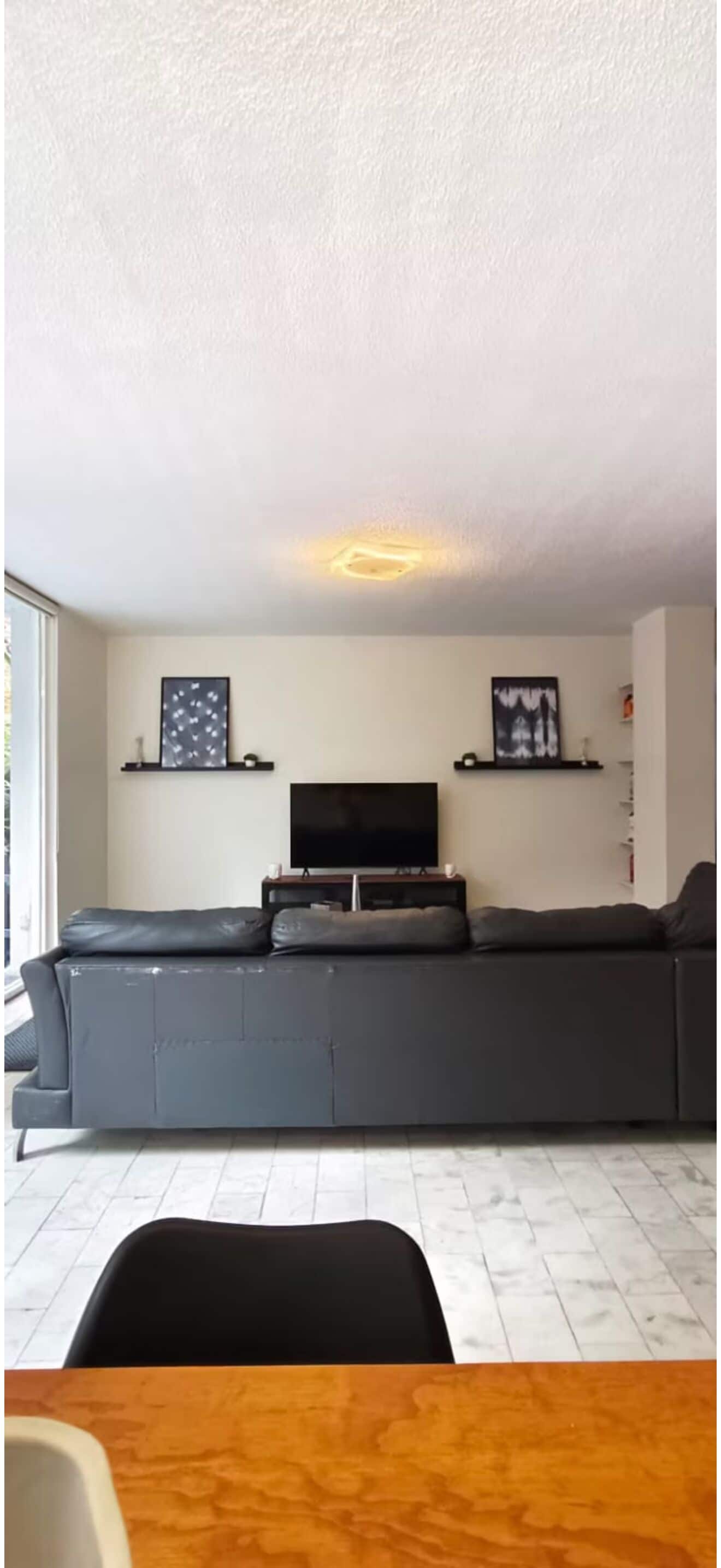 A living room with a grey sofa, a flat-screen TV, and two framed pictures on the wall.