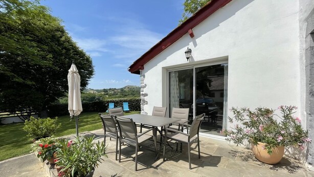 Eine Terrasse mit Tisch und Stühlen, umgeben von Kübelpflanzen und Blick auf die Landschaft.
