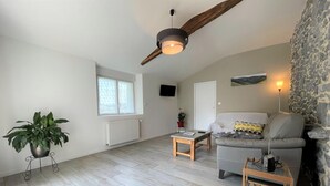 Ein geräumiges Wohnzimmer mit hoher Decke, einer Steinwand, einem grauen Sofa, einem Holztisch und einer Topfpflanze.