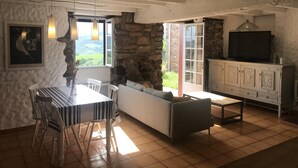 A dining area with a table and chairs, a sofa, a television, and a stone wall. - FAGACHURIA - ITXASSOU (ITXASSOU)