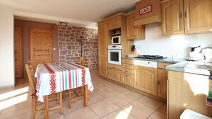 Una cocina con armarios de madera, una mesa de comedor con sillas, una pared de piedra y piso de baldosas.