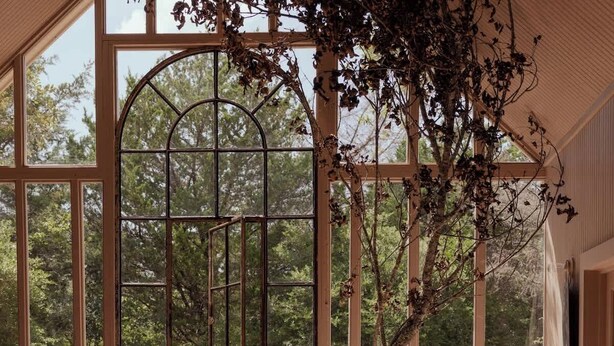 Un comedor rústico con una gran mesa de madera, sillas y vistas a un jardín a través de amplias ventanas.