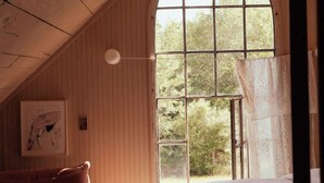 Un dormitorio acogedor en el ático con un gran ventanal de arco, paredes de madera, una cama, una silla y una mesita.