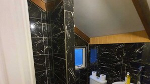 Un baño con paredes de mármol negro, un inodoro blanco, un lavamanos y un ventanal pequeño.