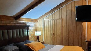Un dormitorio con techo inclinado, paredes de madera, una cama con ropa de cama a rayas, un plaid amarillo y un televisor montado en la pared.