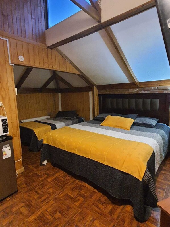 Une chambre avec deux lits, des murs en bois, un plafond en pente et un plancher en bois.