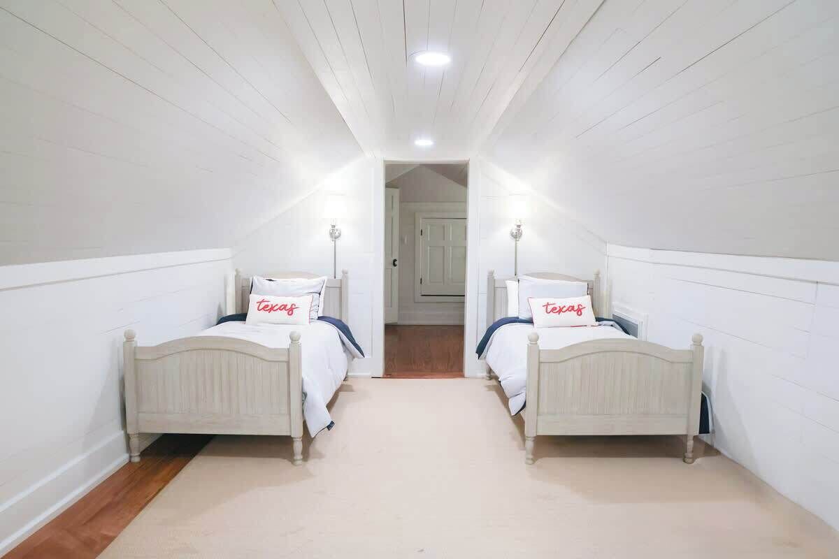 A narrow, white-paneled room with two single beds, each with a pillow labeled "texas."
