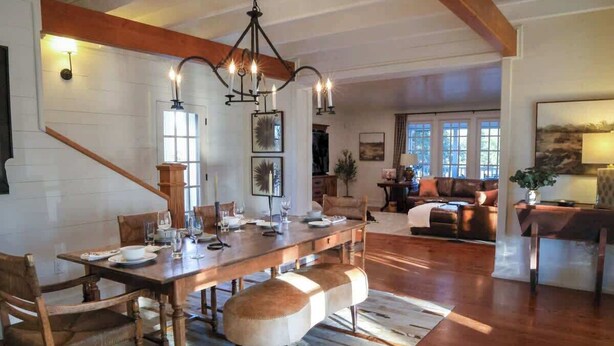 Un amplio salón con una mesa de comedor de madera dispuesta para cuatro personas, un ventanal grande y una zona de estar acogedora con un sofá y sillones.