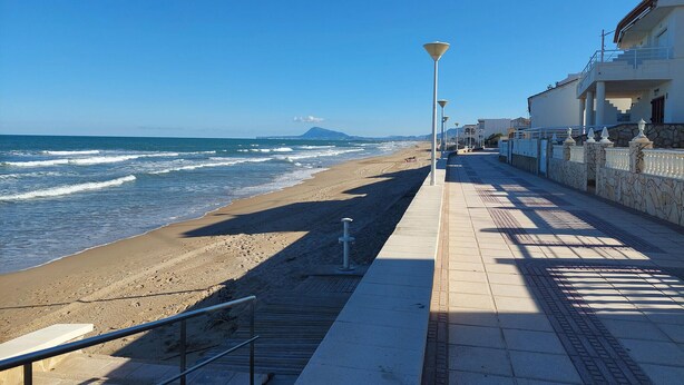 Un paseo marítimo con una playa, un farol y un edificio con balcón.