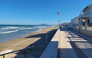 Une promenade en bord de mer avec une plage, un lampadaire et un bâtiment doté d’un balcon.
