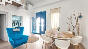 Un comedor con una mesa redonda de madera, sillas blancas y un sillón azul.