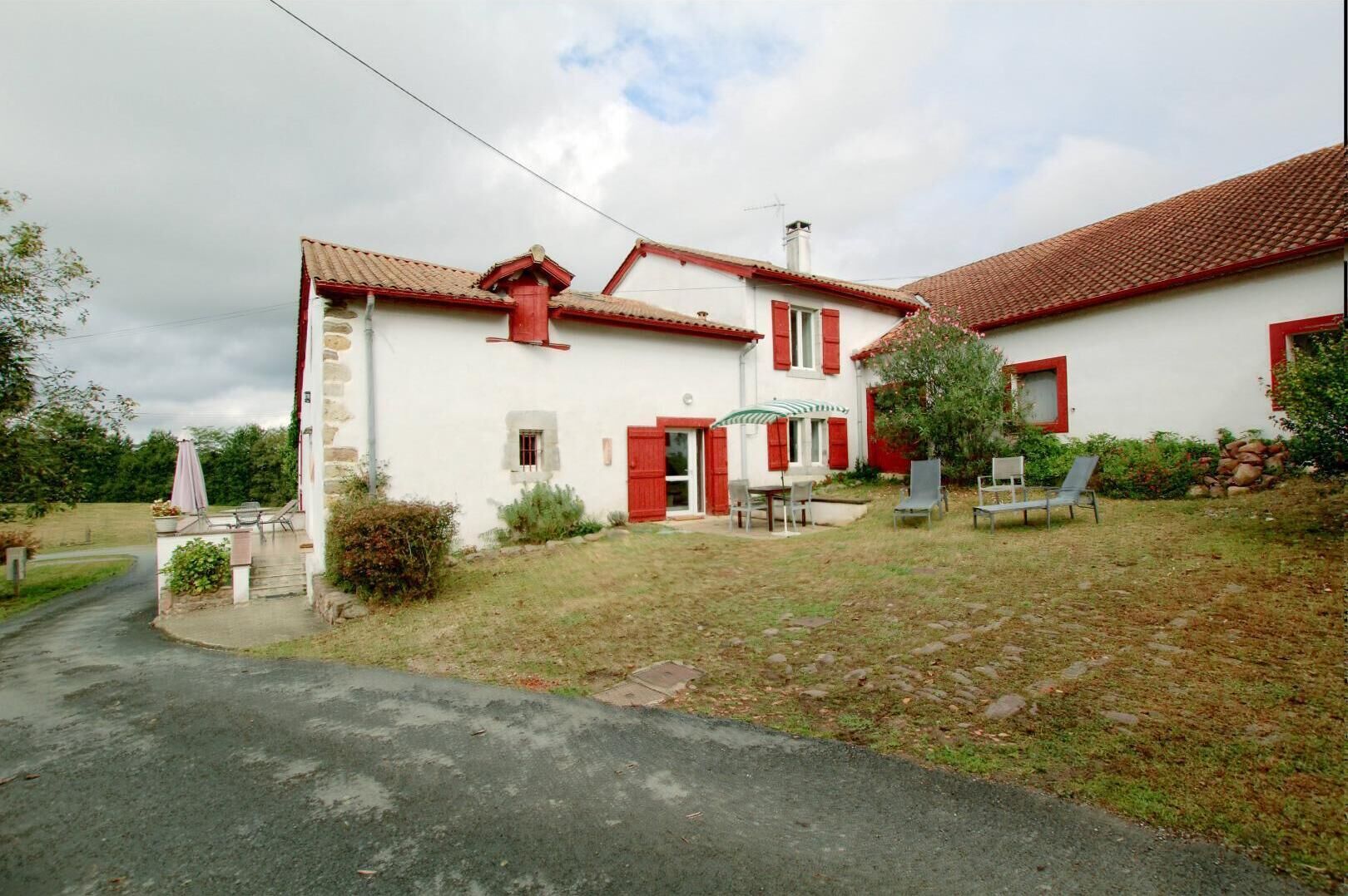 A two-story house with a red-tiled roof, a stone facade, and a small garden with outdoor seating.