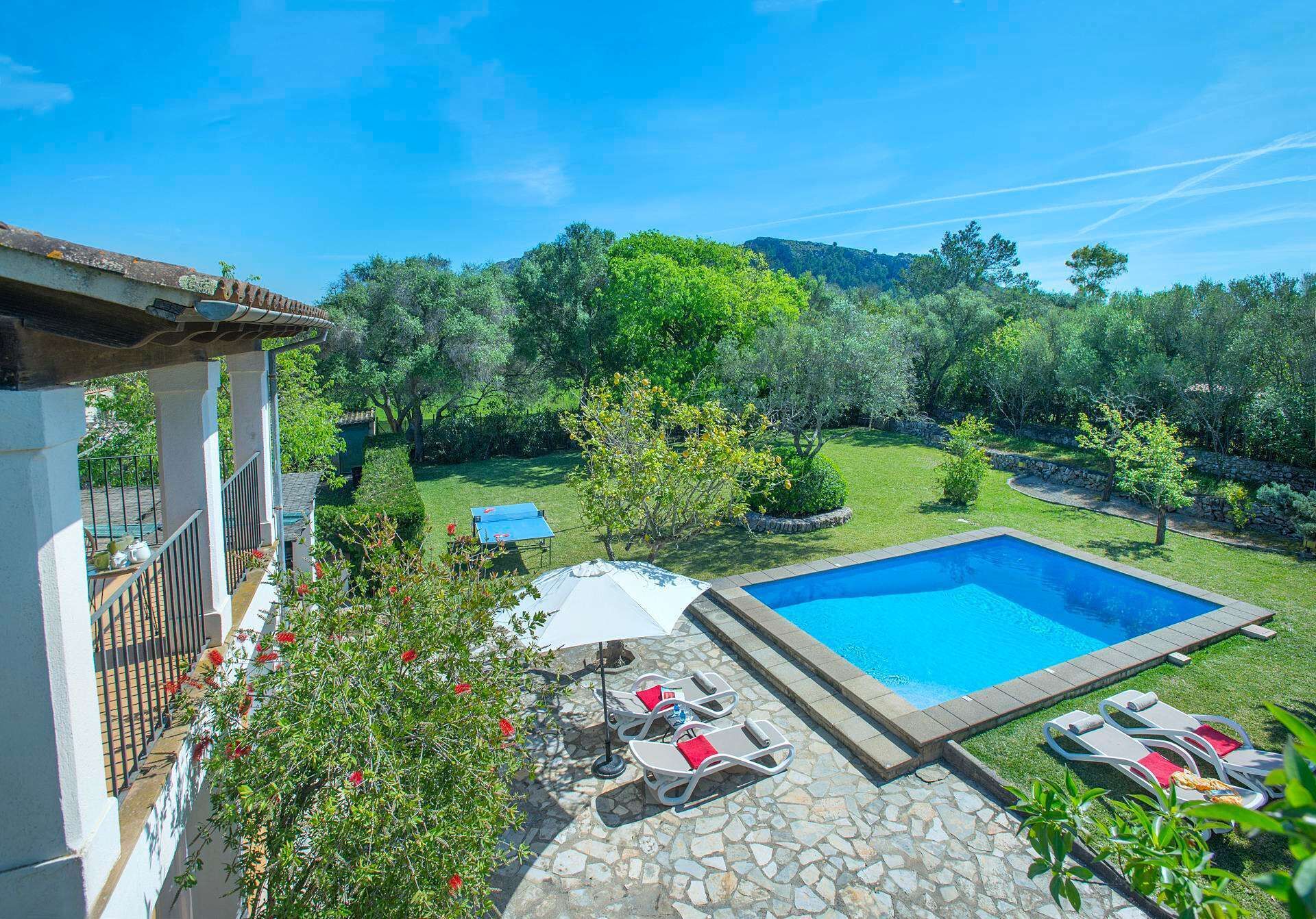 Área de piscina com deck de pedra, espreguiçadeiras e vista para um jardim e floresta exuberantes.