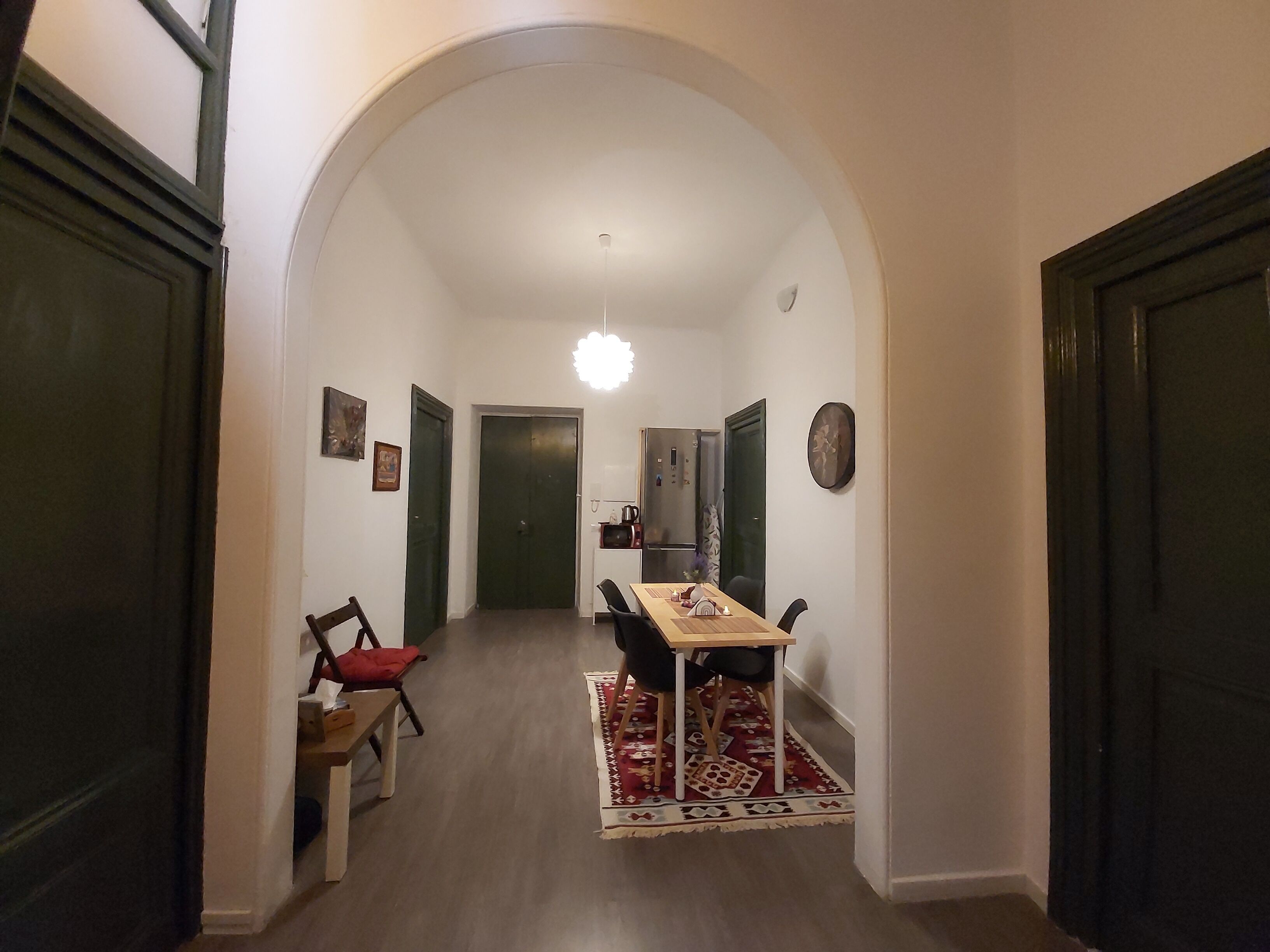 A hallway with a dining area featuring a table and chairs, a rug, and a ceiling light.