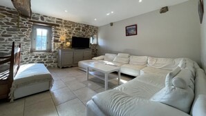 A living room with a stone wall, a white sofa, a TV, and a window. - MARTIN AUNDIENIA - SARE (SARE)