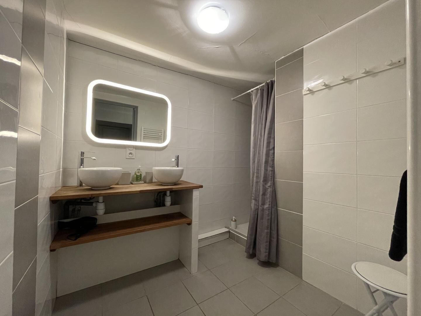 A modern bathroom with two sinks, a mirror, a shower curtain, and a small table.