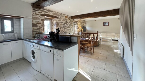 A kitchen with stone walls, a built-in washing machine, and a dining area with a table and chairs. - MARTIN AUNDIENIA - SARE (SARE)