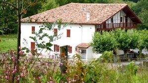 A white building with a red-tiled roof and a balcony, surrounded by greenery and a fence. - MARTIN AUNDIENIA - SARE (SARE)