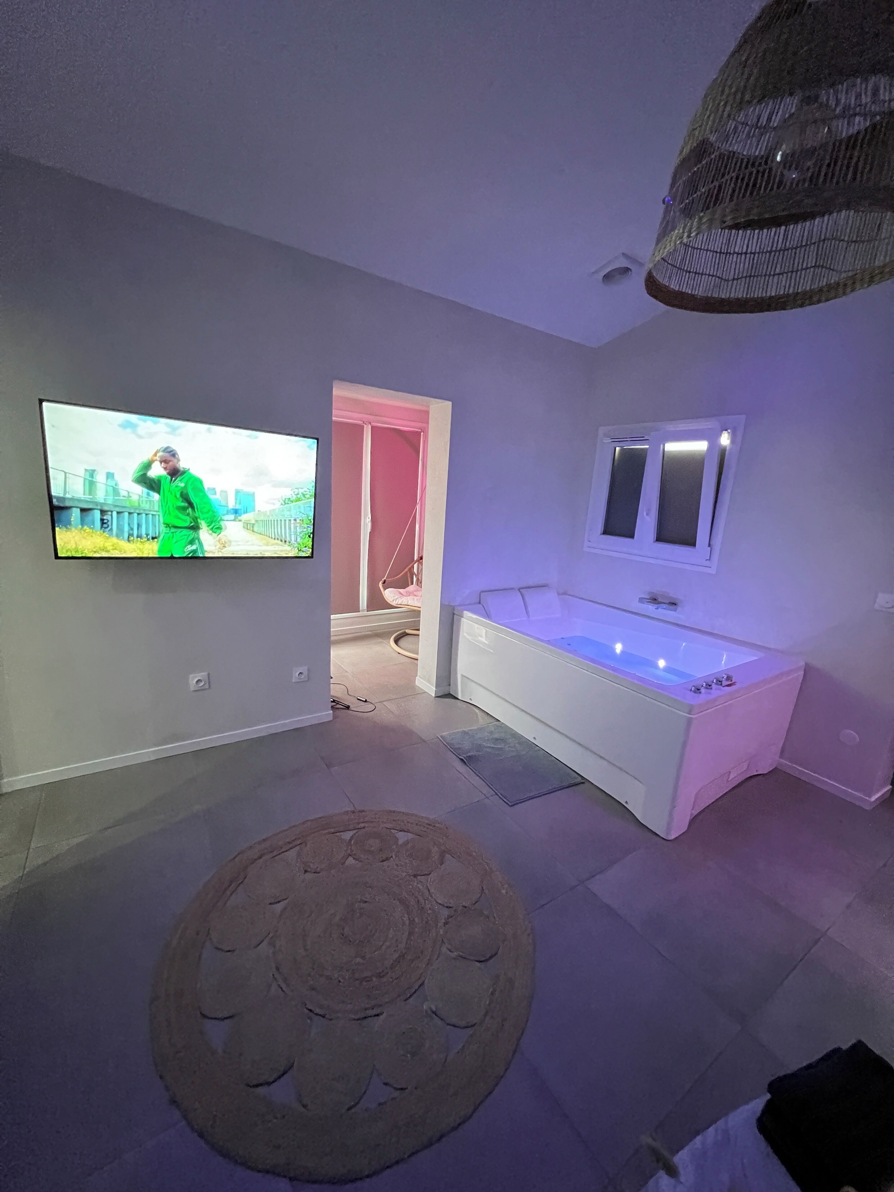 Ein modernes Badezimmer mit einer weißen Badewanne, einem großen Spiegel und einem an der Wand befestigten Fernseher.