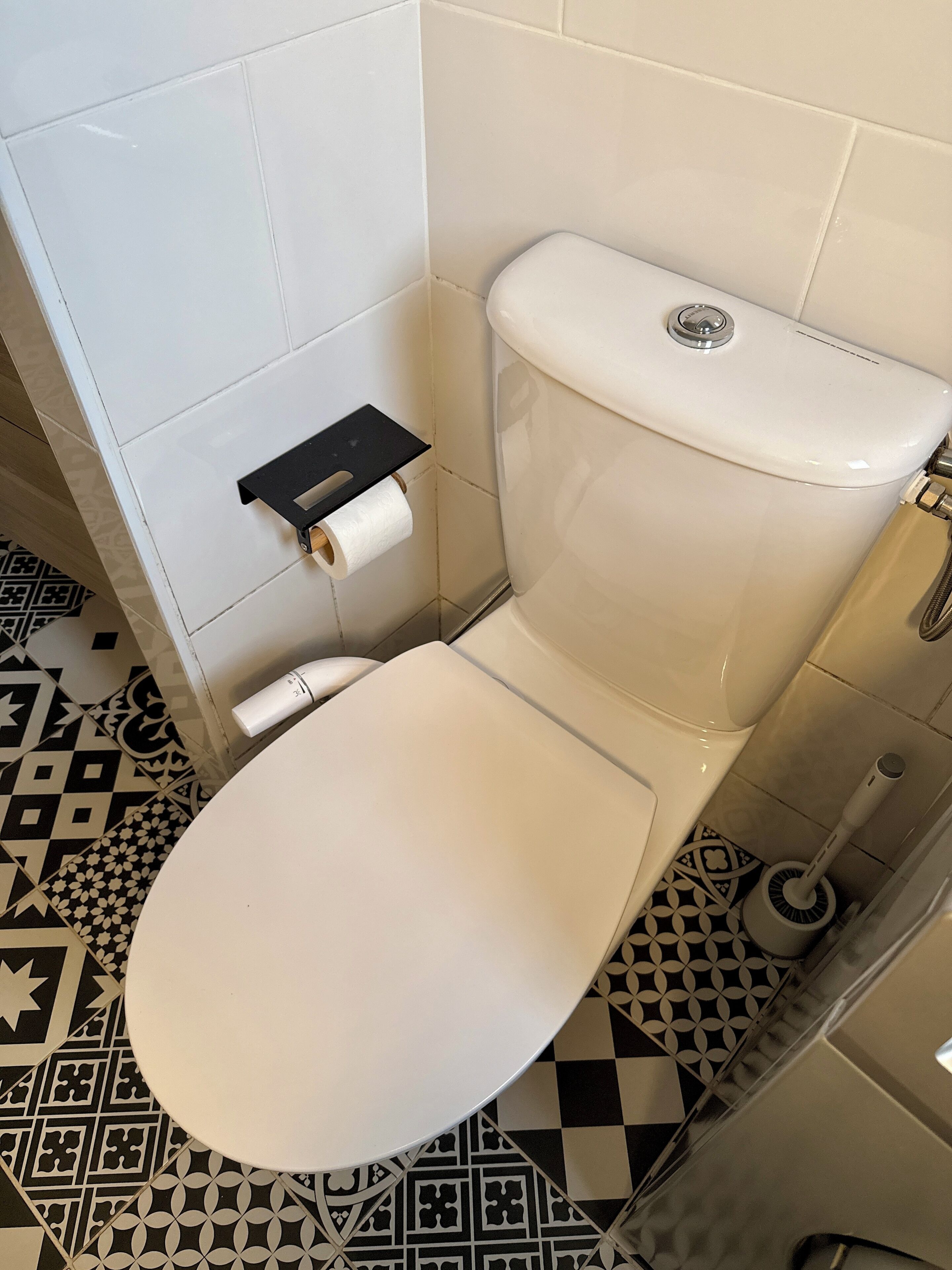 Un inodoro con asiento y tanque blancos, un dispensador de papel higiénico y un suelo con diseño.