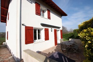Un edificio bianco con persiane rosse, un patio in pietra e mobili da esterno.