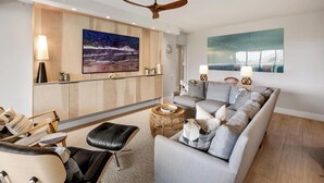 Ein modernes Wohnzimmer mit grauem Sofa, einem schwarzen Ledersitzhocker, einem Holztisch und einem Deckenventilator.