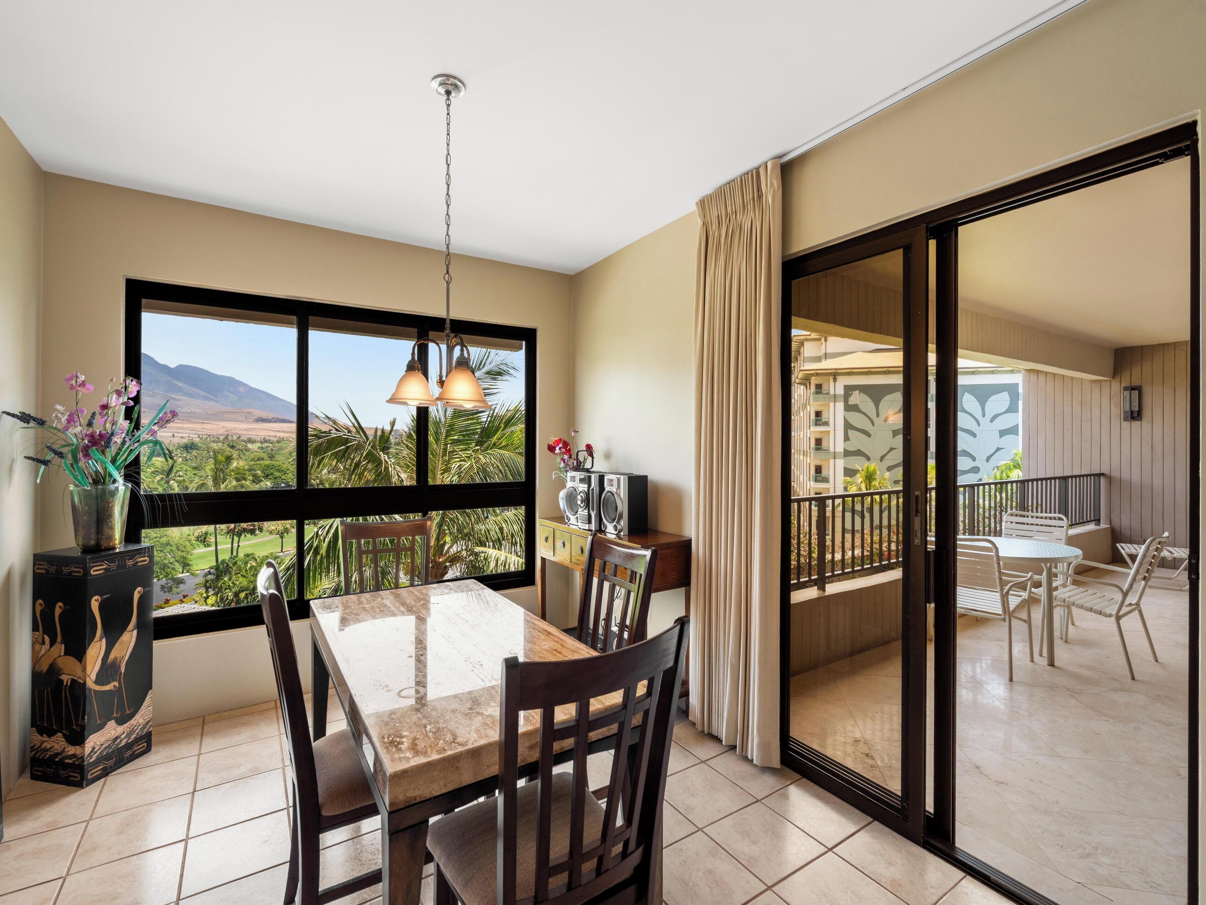 A dining area with a table and chairs, a view of mountains through large windows, and a balcony with chairs.